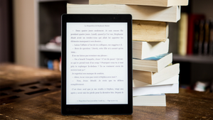 An eReader and stack of books.